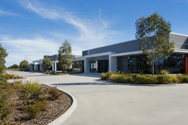 A low commercial building in a suburban business estate: grey rendered walls, a covered entry canopy, native planting and a wide concrete driveway.