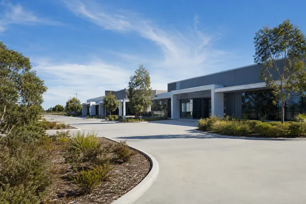 The same style of suburban commercial building seen from the driveway, with eucalypts and low shrubs along the kerb.