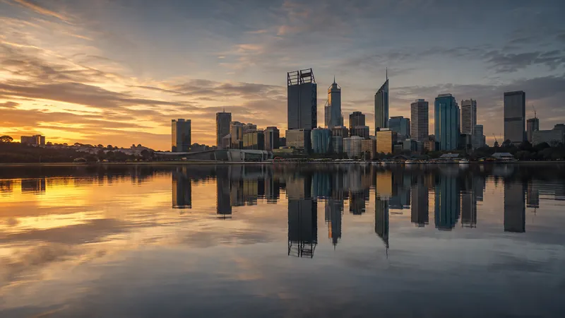 The Perth city skyline at sunrise, mirrored in the still water of the Swan River.